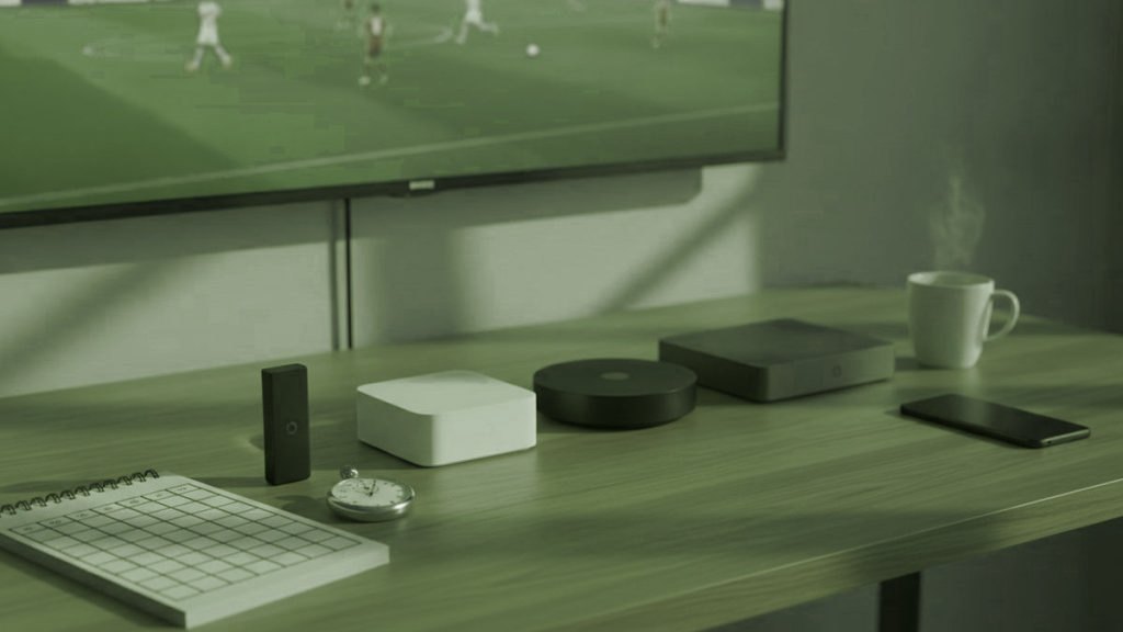Cinq appareils de streaming, une grille de notation et un chronomètre devant un téléviseur diffusant un match de football
